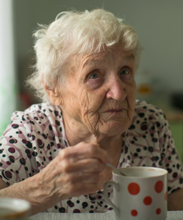 Äldre kvinna sitter i sitt kök och dricker te. 
